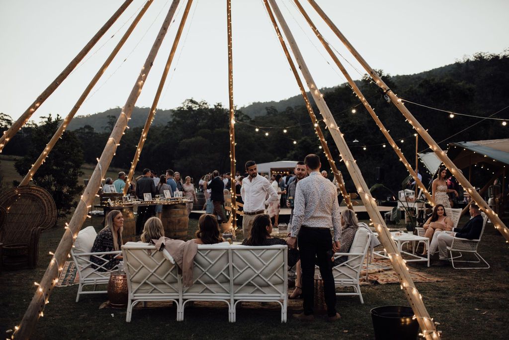 Wedding guests sitting down on chairs and standing under a tipi