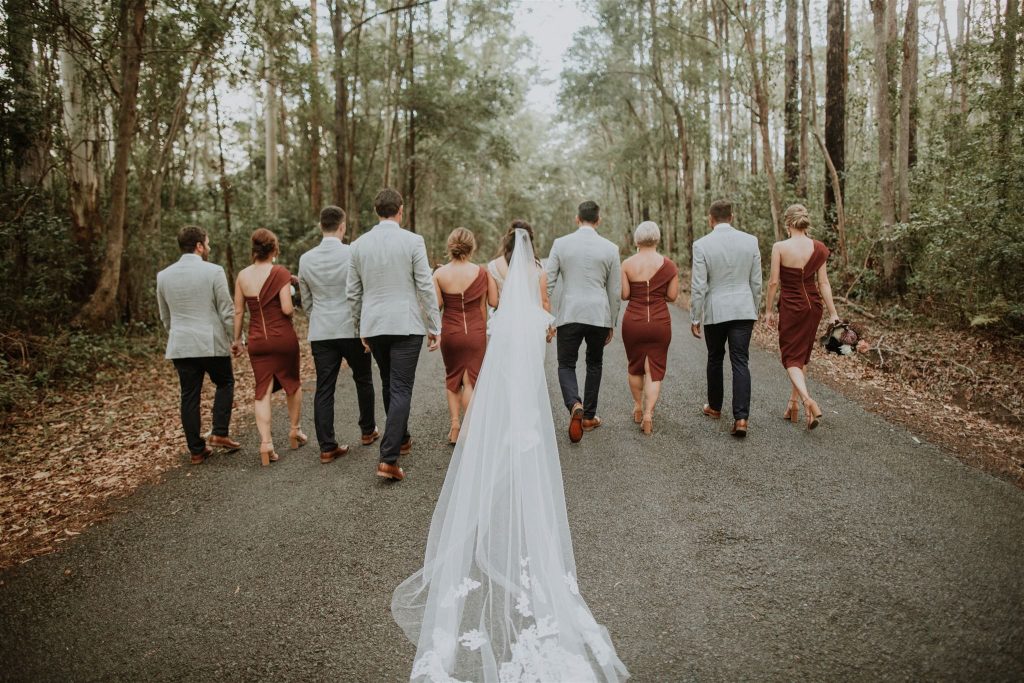 Wedding party walking through forest with backs turned away from camera
