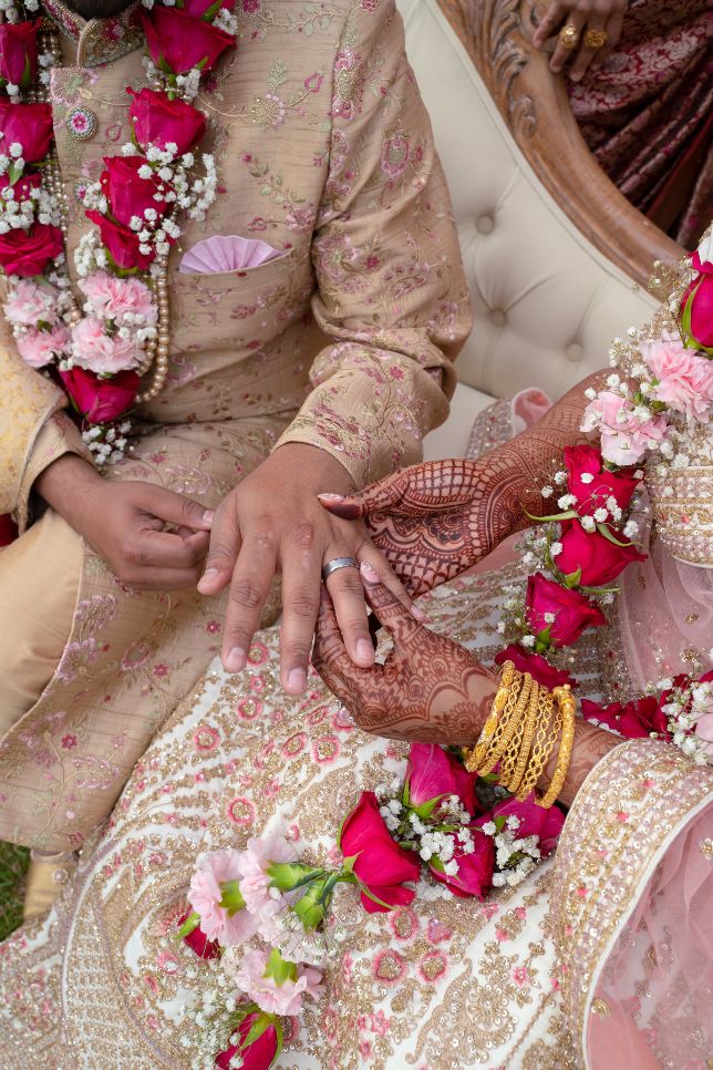 Couples hands featuring traditional henna art, jewellery and flowers