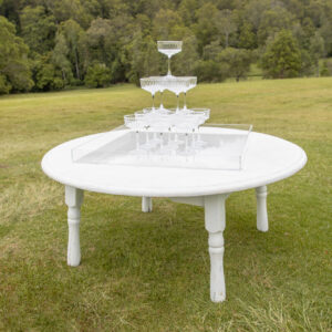 White round table holding champagne tower with clear tray underneath