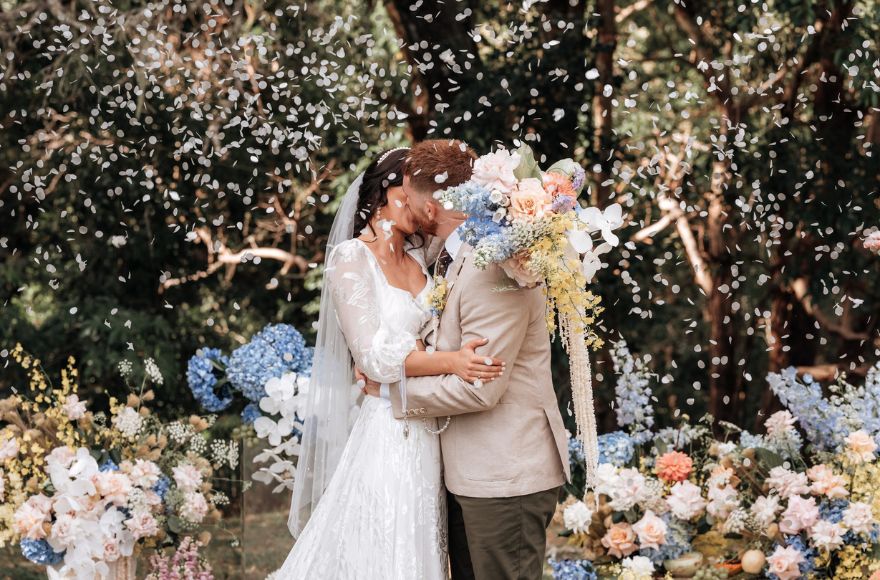 Bride and groom share first kiss as flower petal confetti is thrown on them