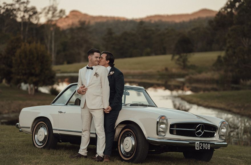 Newly wed husbands pose together by a vintage Mercedes on the Farm House grounds