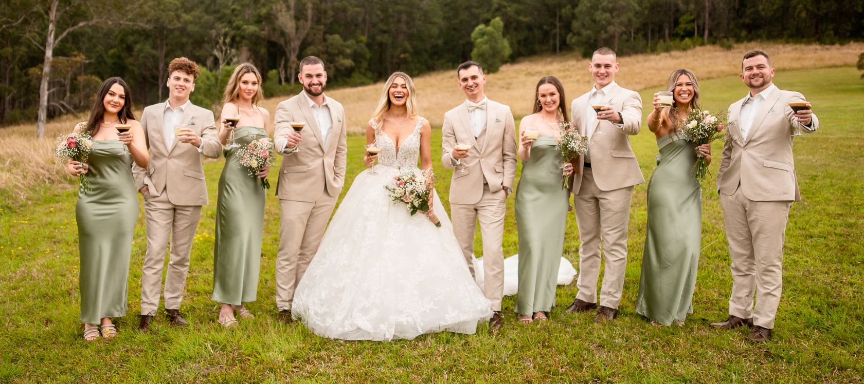 Bridal party pose with cocktails wearing a colour palette of sage green and neutrals