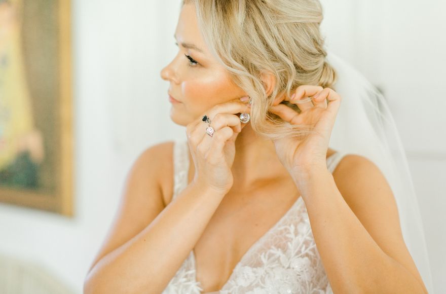 Bride puts her earrings on; wears vintage wedding rings 