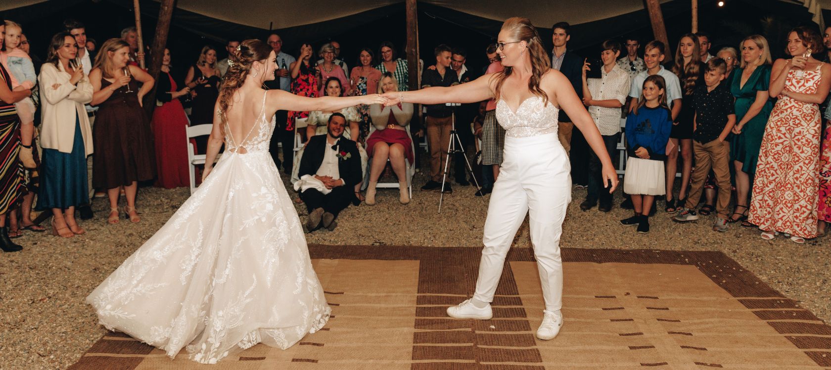 Two brides dance their first dance together as wedding guests watch on
