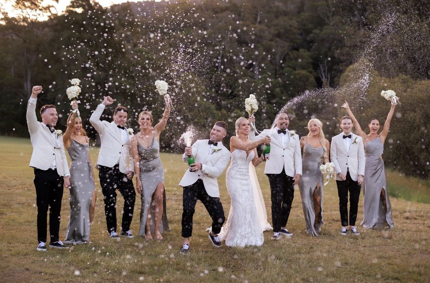 A wedding party celebrate as the bride and groom pop bottles of champagne .