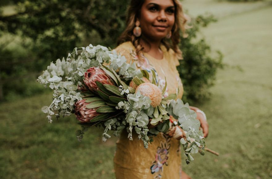 bride holds a sheath style bouquet of proteas and native Australian folliage. 