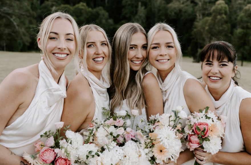 A bride and her bridesmaids pose together with bouquets of white and pink flowers