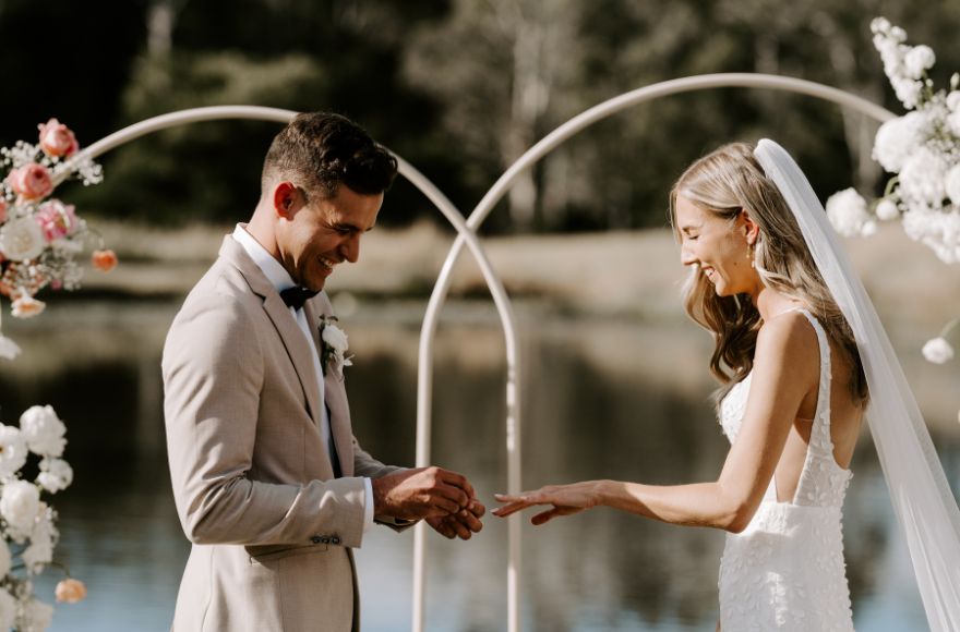 Groom puts ring on bride's finger at their lakeside wedding ceremony