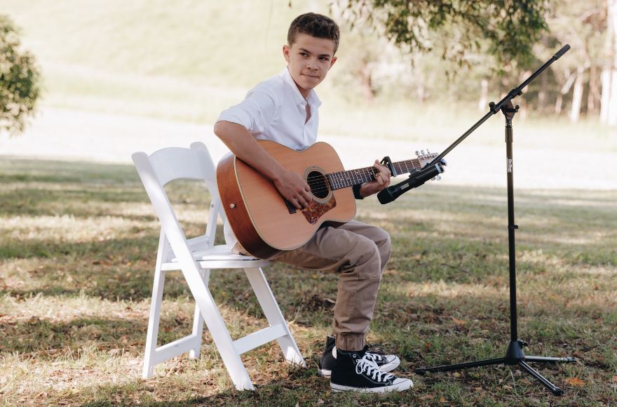 Boy plays acoustic guitar at intimate outdoor wedding