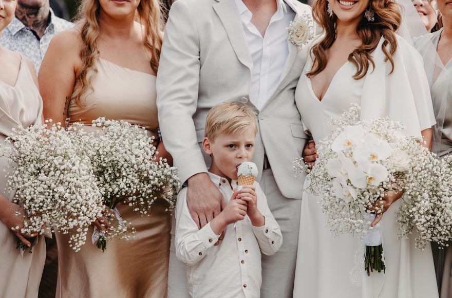 Little boy poses with his newlywed parents. He is eating an icecream. 