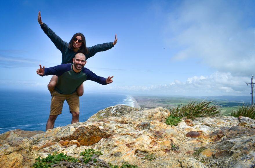 Man piggybacks woman as they stand on a mountain peak