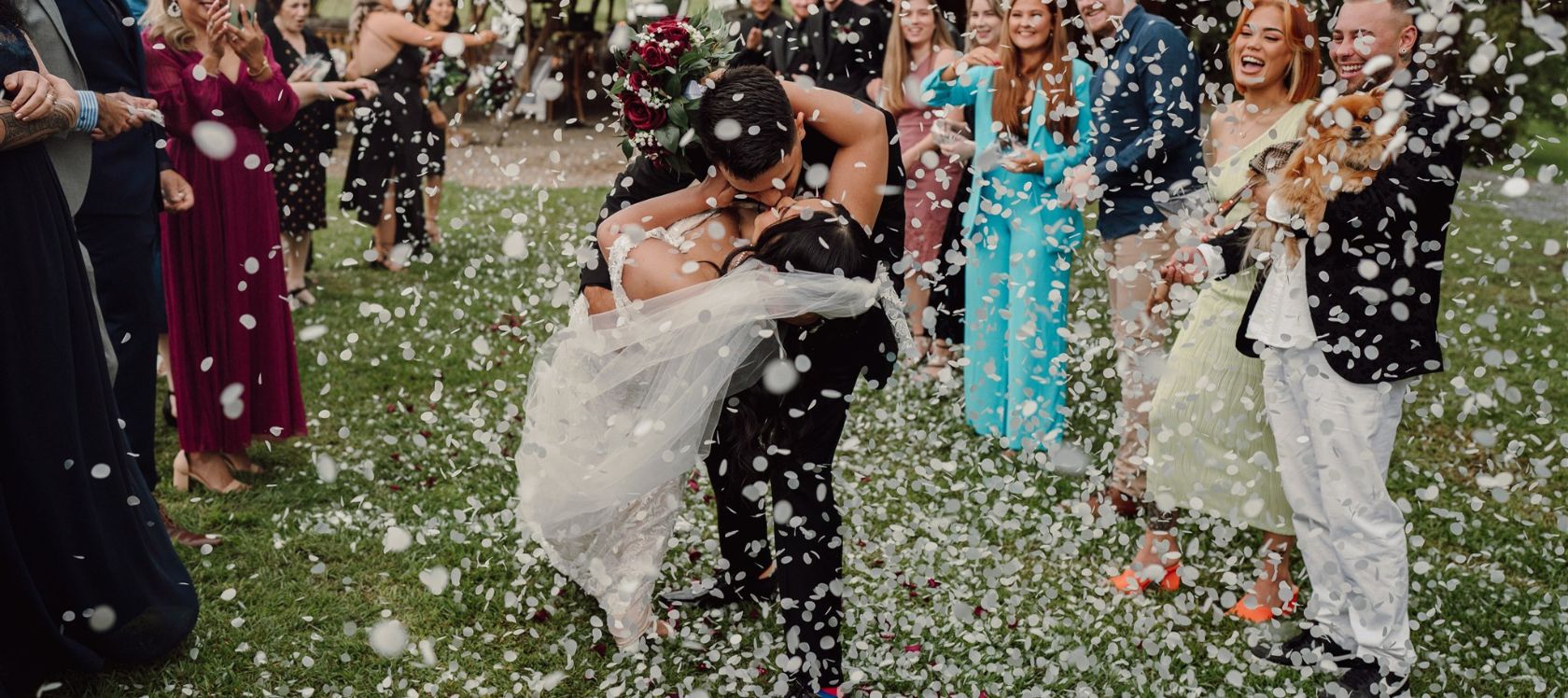 Bride and groom embrace and kiss as confetti is thrown on them