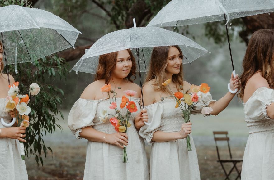 Bridesmaids stand under clear umbrellas during a raining wedding ceremony