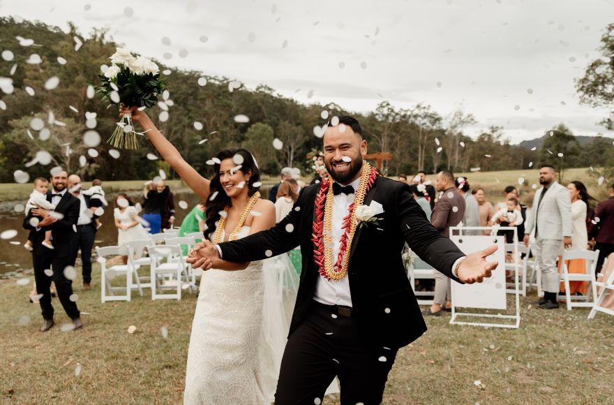 Bride and groom celebrate after their wedding ceremony as white paper confetti is thrown on them 