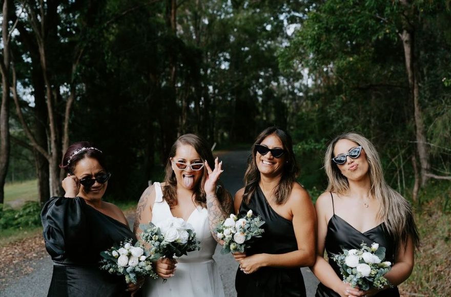 A bride wearing white poses with her 3 bridesmaids dresses in black