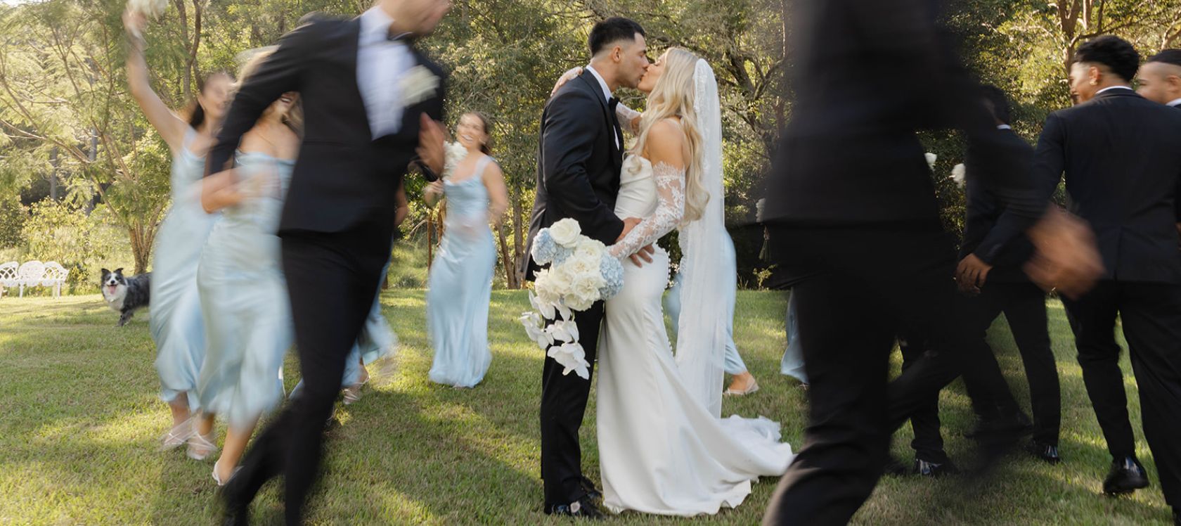 Bride and Groom share a kiss while their bridal party mingle around them